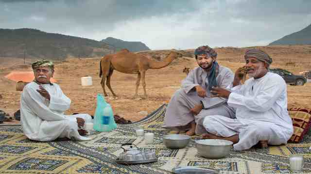 Dhofar-Salalah-Oman-Three-men-are-having-refreshment-in-front-of-theit-tent-Tea-and-camel-milk-is-available-A-camel-is-standing-on-the-back