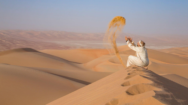 Next travel destination Oman affordable vacation Planning Service and Company 6 Man-in-traditional-outfit-in-a-desert-at-sunrise-throwing-sand